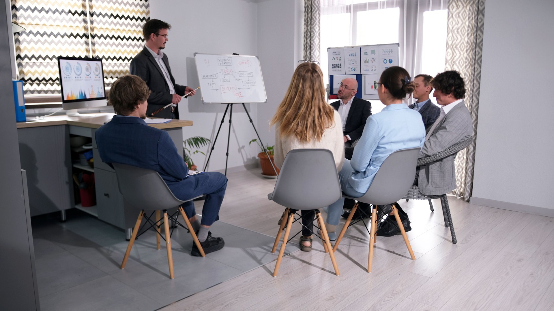 The mentor conducts training in the company of business people. A group of people are sitting on chairs in a conference room